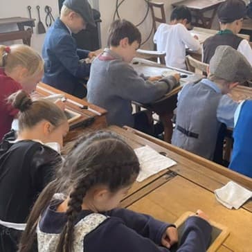 A photo of children in a classroom doing some schoolwork, each sat at a desk.