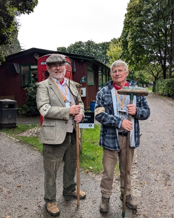 Two volunteers holding brooms and smiling.