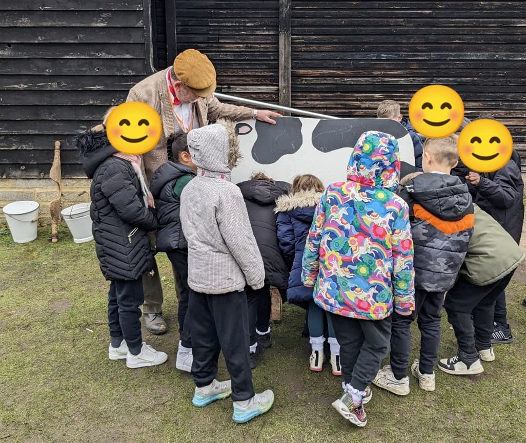 Children standing around a wooden cow, pretending to milk it.