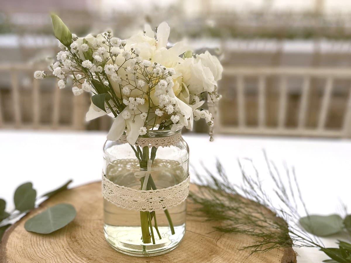 A white flower in a mason jar atop a wood plate.